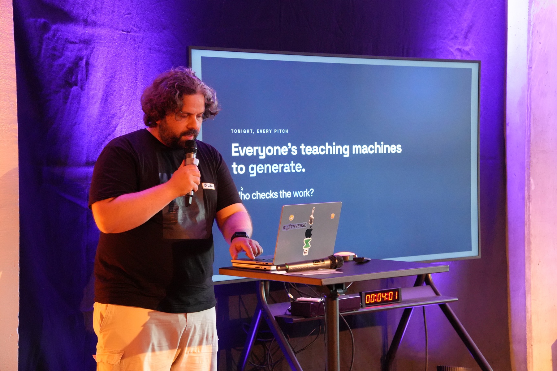Ruslan Strazhnyk presenting the QualityMax thesis at Berlin SaaS Night, with the question Who checks the work displayed behind him